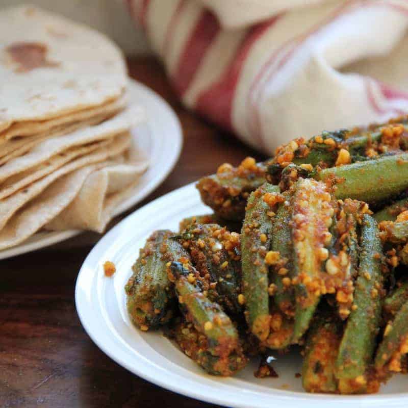 Stuffed Okra in a white platter with Indian roti's on the side in a white plate.
