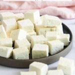 A plate of freshly made paneer cubes sits on a white surface, with some cubes scattered nearby. Text at the top advertises fresh homemade paneer with two ingredients and no preservatives.