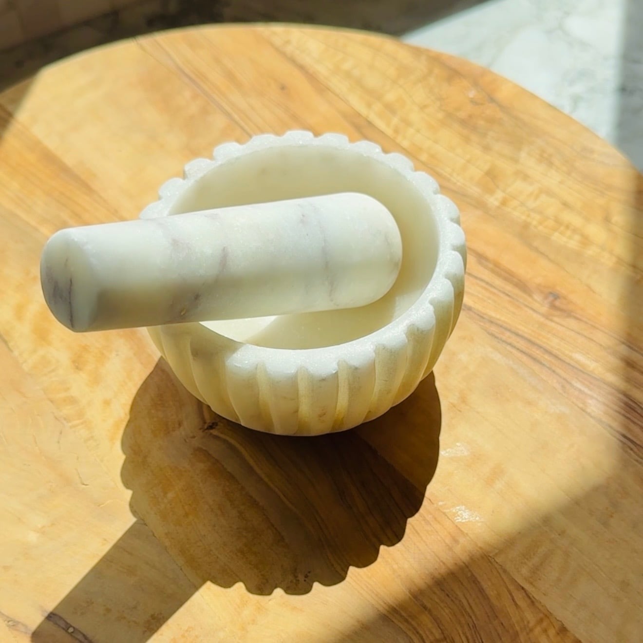 White marble mortar and pestle resting on a wooden surface, with sunlight casting shadows across the scene.