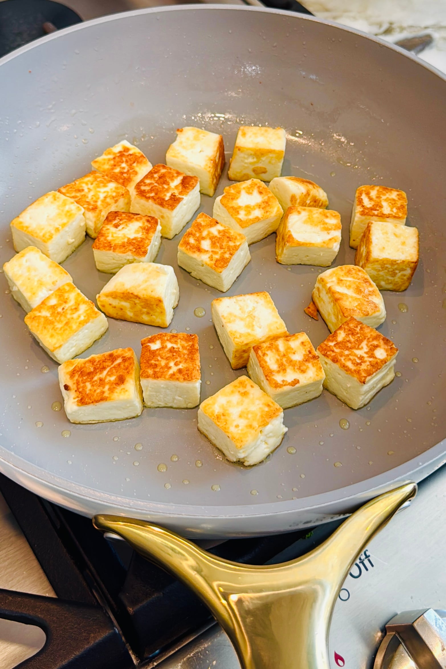 Cubed pieces of paneer are being pan-fried in a nonstick skillet, turning golden brown on multiple sides.
