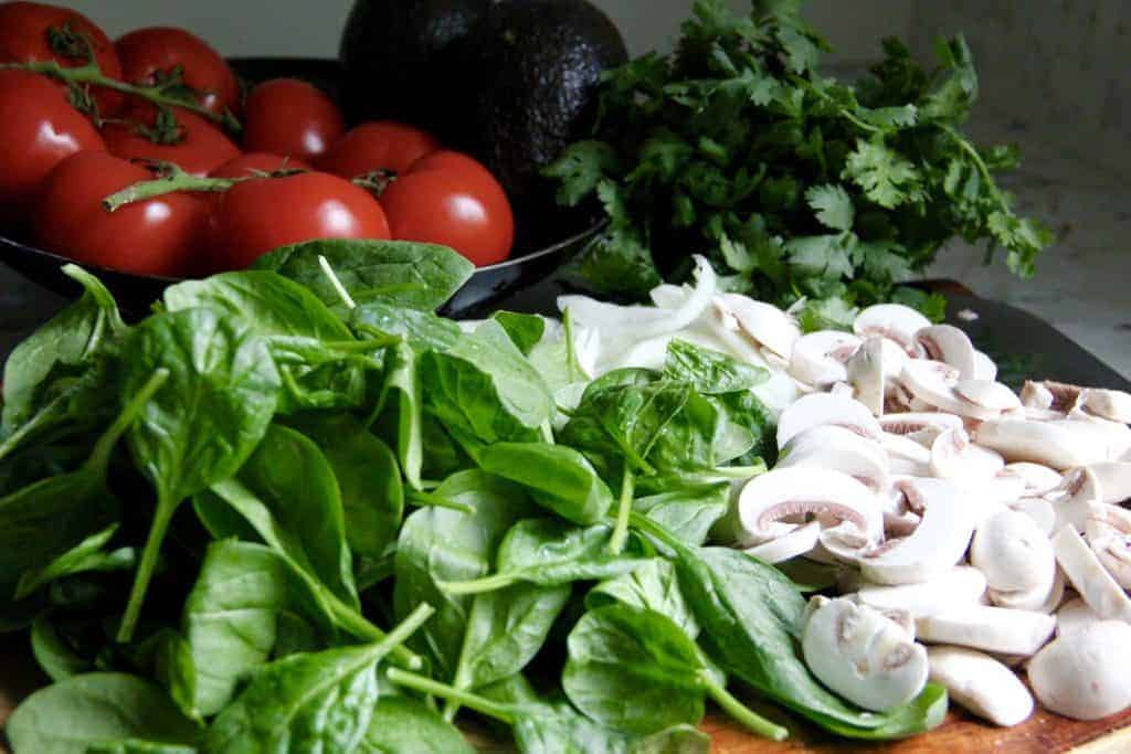 spinach, mushrooms , tomatoes and cilantro on a cutting board 