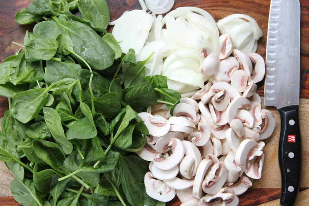 baby spinach, sliced mushrooms and onions on a wooden cutting board 