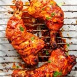 Three pieces of tandoori chicken on a wire rack, garnished with herbs, with oven-grilled marks and visible spices.