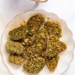 Plate of sliced Kothimbir Vadi, a green cilantro snack garnished with sesame seeds, on a white plate. Text above describes it as a traditional Maharashtrian cilantro snack.