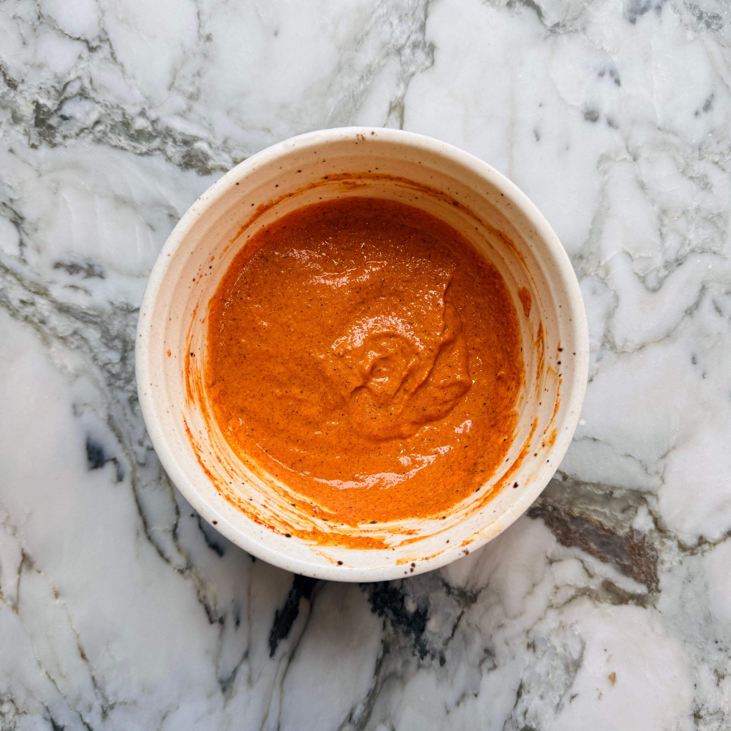 A white bowl filled with thick, yogurt marinade with spices.