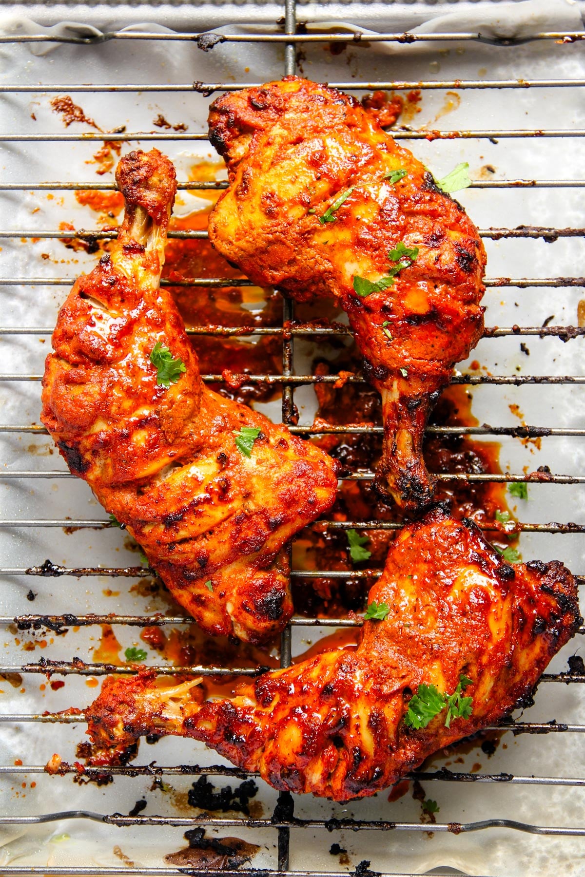 Three seasoned, grilled chicken leg quarters on a wire rack over a baking sheet, garnished with a few sprigs of parsley.