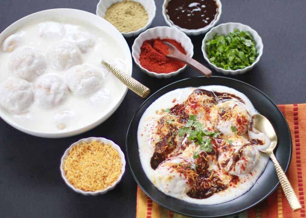 Dahi vada with garnish served in a black plate with spoon. 