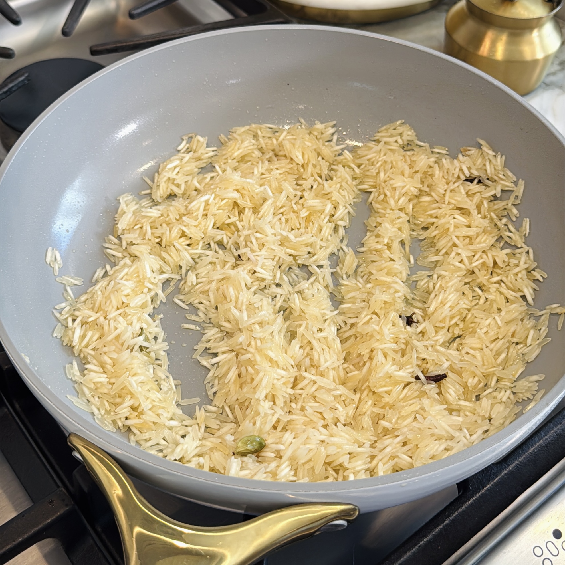 Uncooked rice being sautéed with spices in a light gray pan on a stovetop.