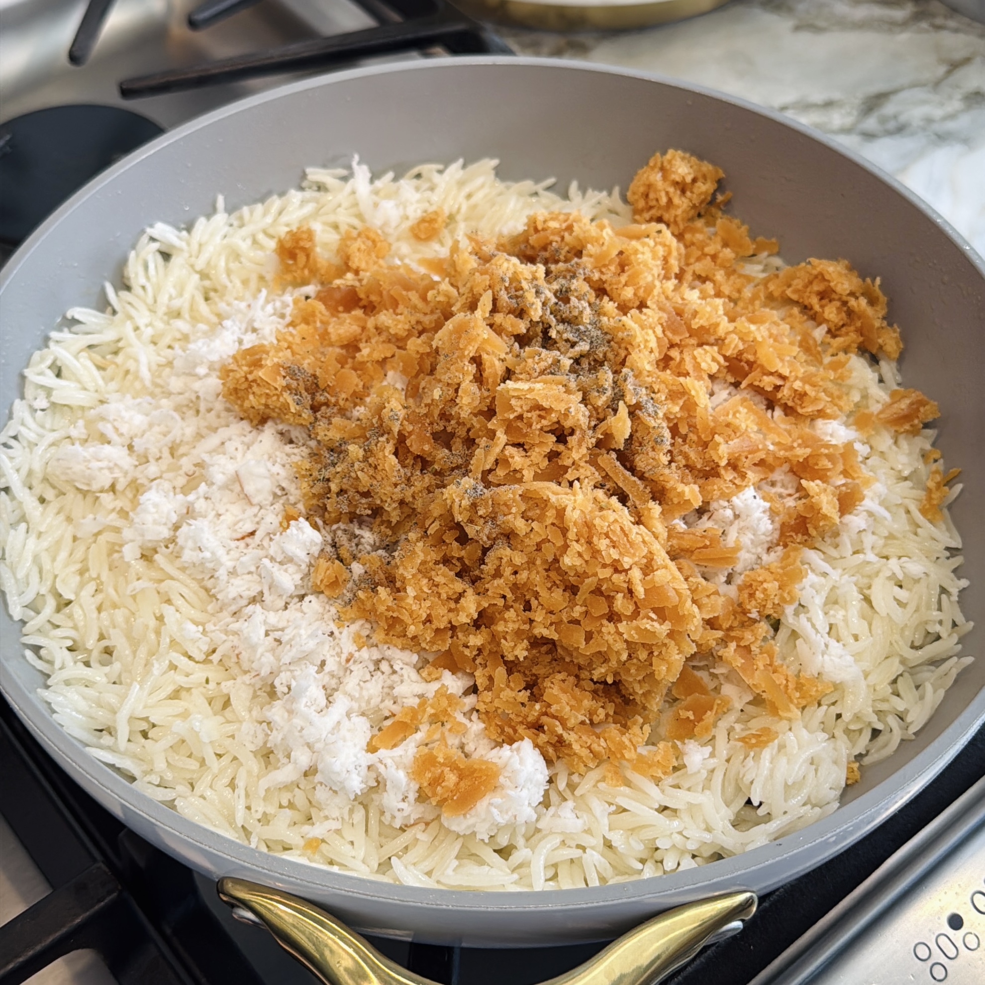 Cooked white rice in a pan topped with grated coconut and jaggery, on a stovetop.