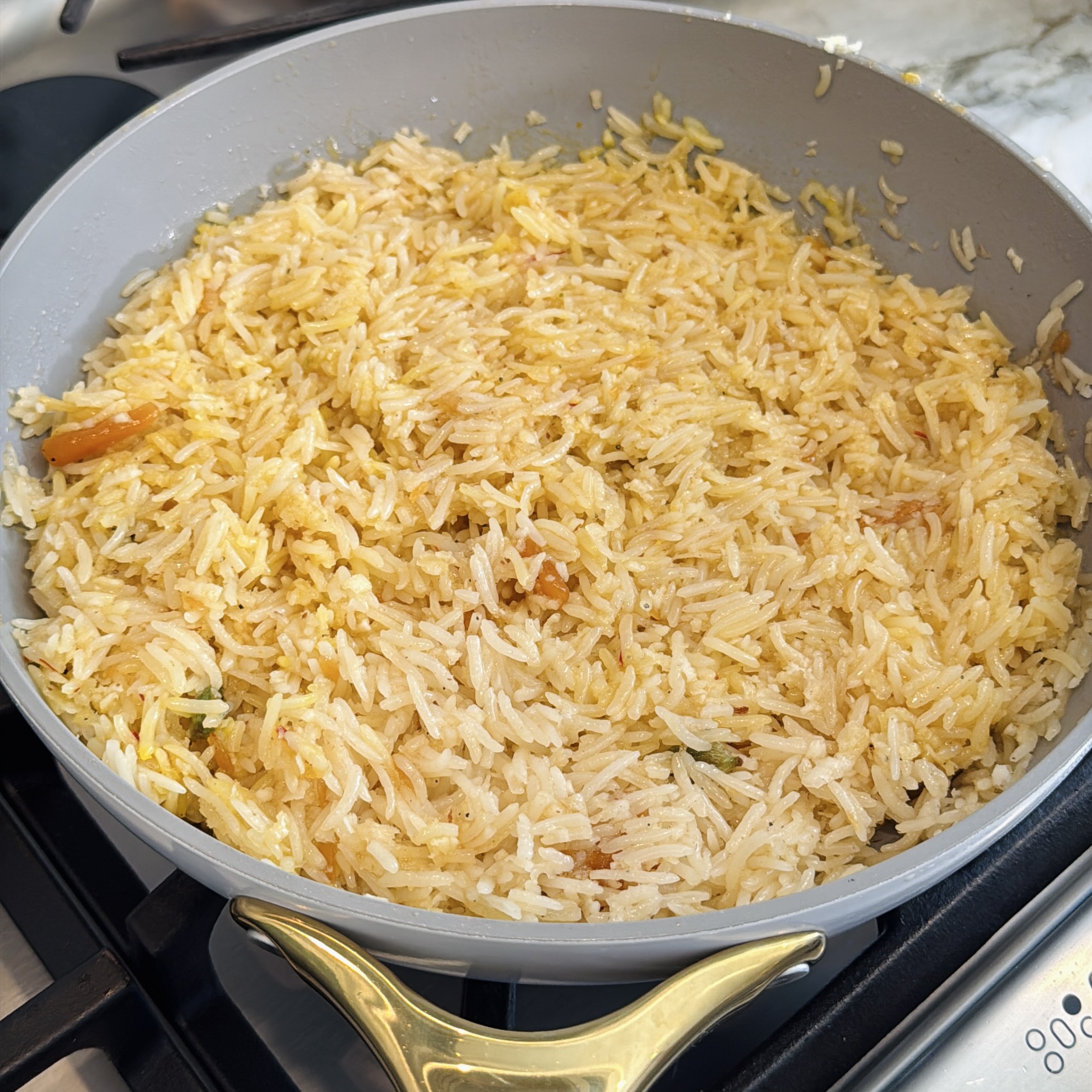 A large pan filled with cooked yellow rice sits on a stove.