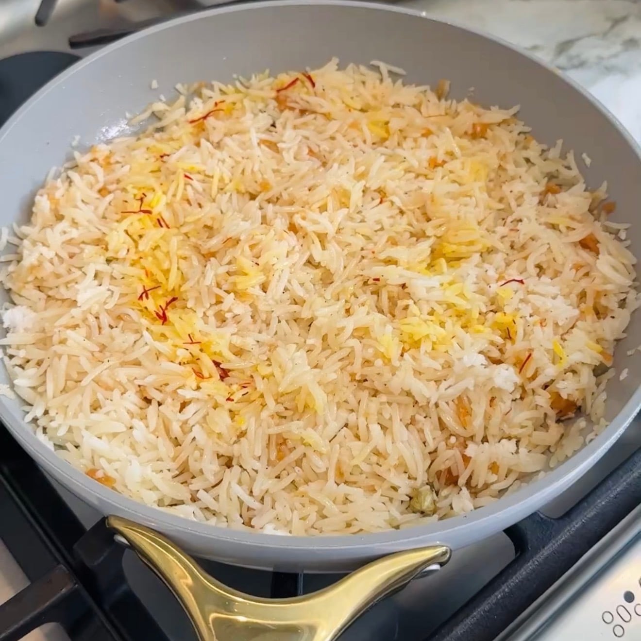 Cooked basmati rice with saffron threads in a gray pan on a stove.
