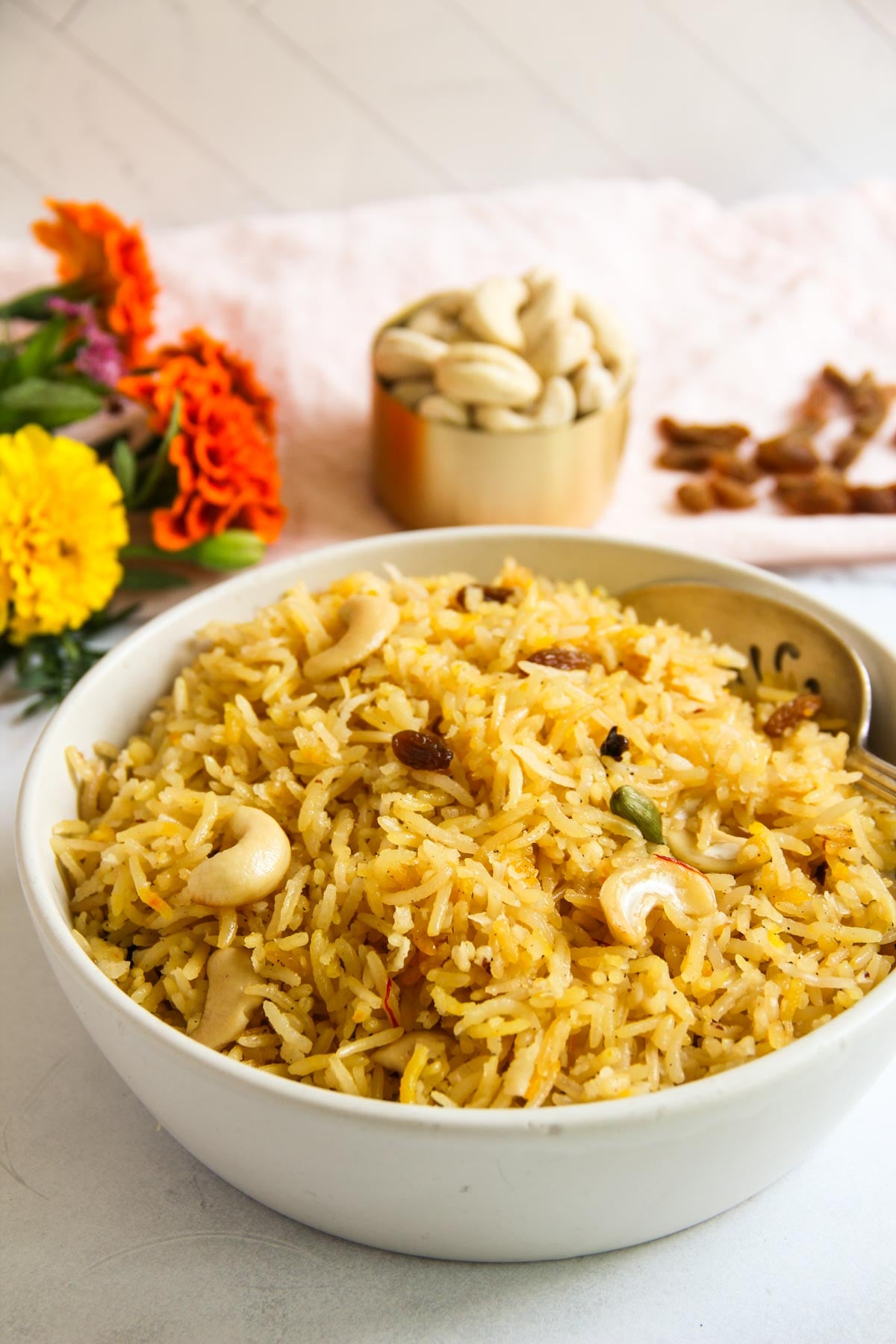 A bowl of narali bhat (sweet coconut rice) garnished with cashews and raisins, with a spoon inside.