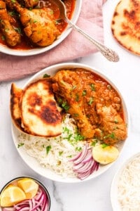 chicken korma served in a white bowl with naan and rice
