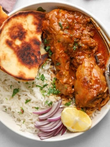 chicken korma in s white bowl with rice and naan