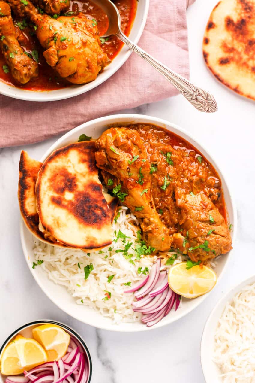 chicken korma served in a white bowl with naan and rice