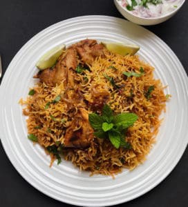Chicken Biryani Served in a dinner plat with a bowl of raita on the side.