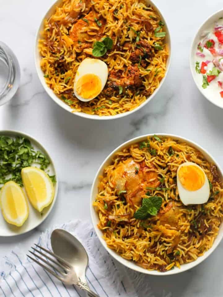 Chicken Biryani served in 2 bowls with raita and lemon wedges