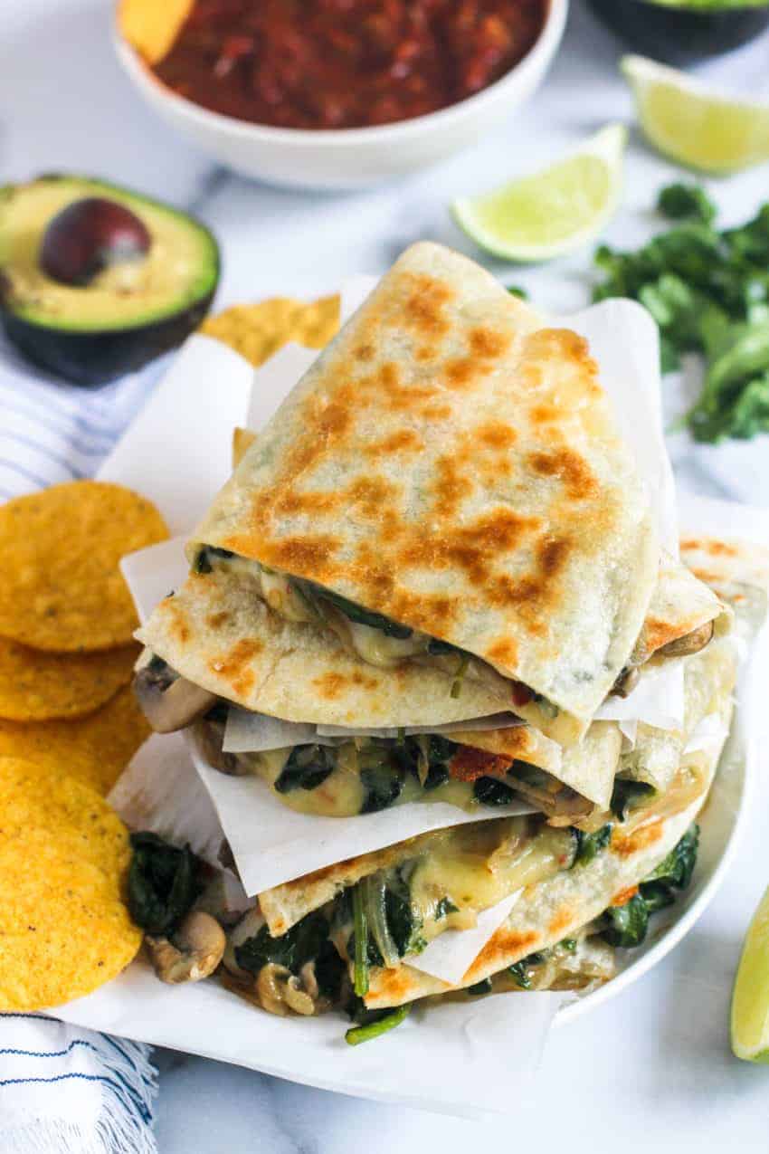 stack of spinach and mushroom quesadiilas with chips, avocado and lime on the side