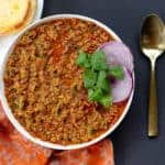 serving bowl with chicken kheema , garnished with cilantro and red onions. Toasted roll on the side.