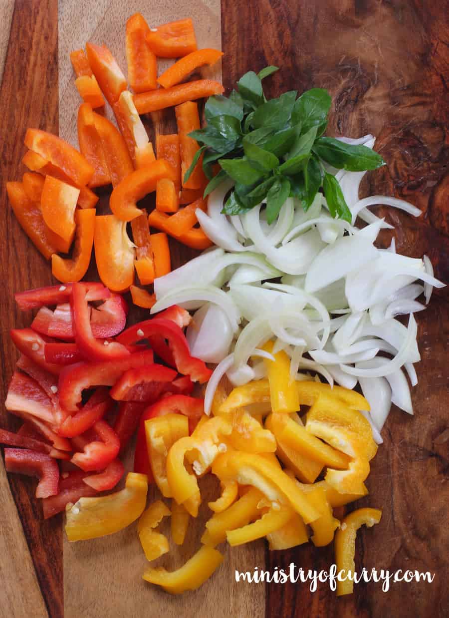 Mixed peppers and onions sliced on a wooden board with basil leaves 