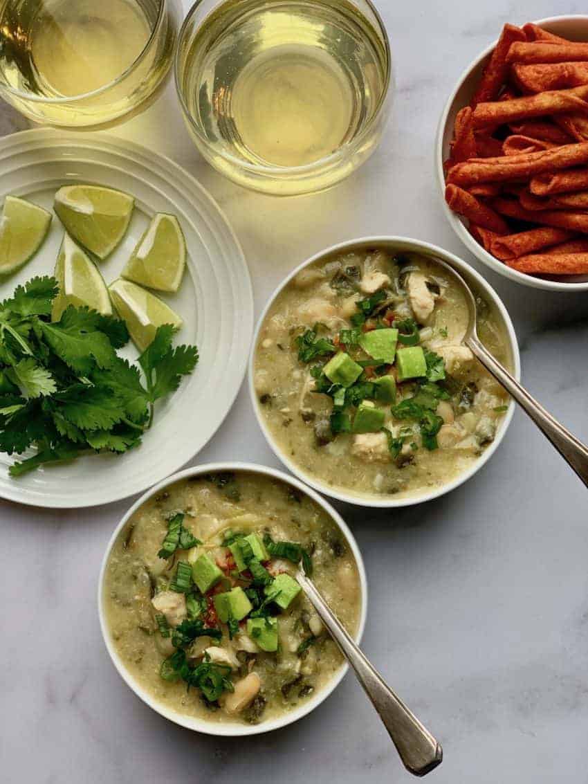 two bowls of white chicken poblano chili with spoons in them