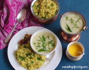 White dinner plate with khichdi and pickle served woth a bowl of kadi. Also a serving bowl of khichdi, kadhi and ghee on the outside