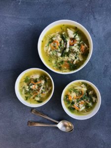 Three white bowls with chicken coriander soup and 2 spoons next to them