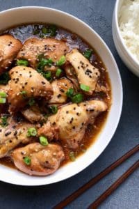 Chicken Teriyaki served in w white bowl garnished with sesame seeds and scallions