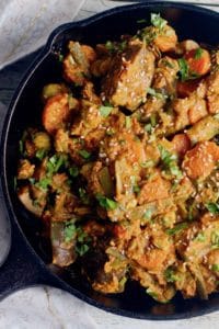 Cast Iron pan with mixed vegetable curry garnished with cilantro and sesame seeds