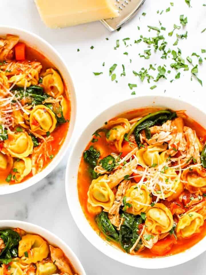 three white bowls with tortellini soup