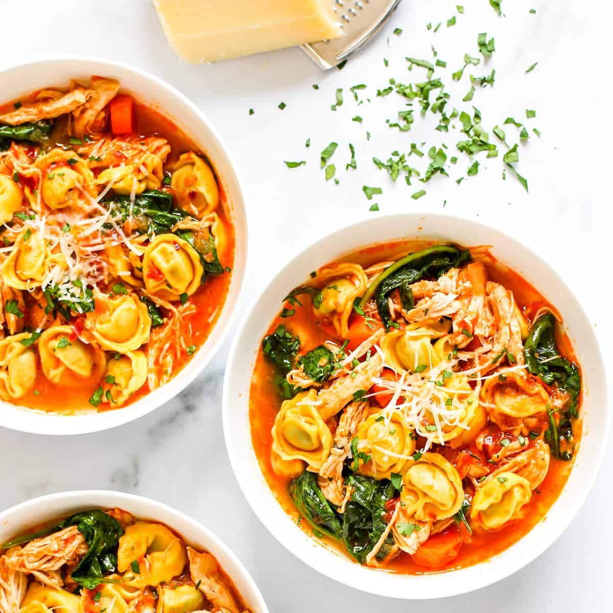 three white bowls with tortellini soup