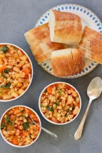 3 white bowls with Pasta e Fagioli soup and a platter of sliced baguette
