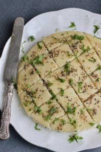 White Platter with savory semolina cakes, garnished with tempered mustard seeds, sesame seeds and cilantro