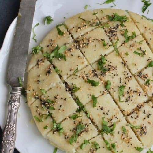 White Platter with savory semolina cakes, garnished with tempered mustard seeds, sesame seeds and cilantro