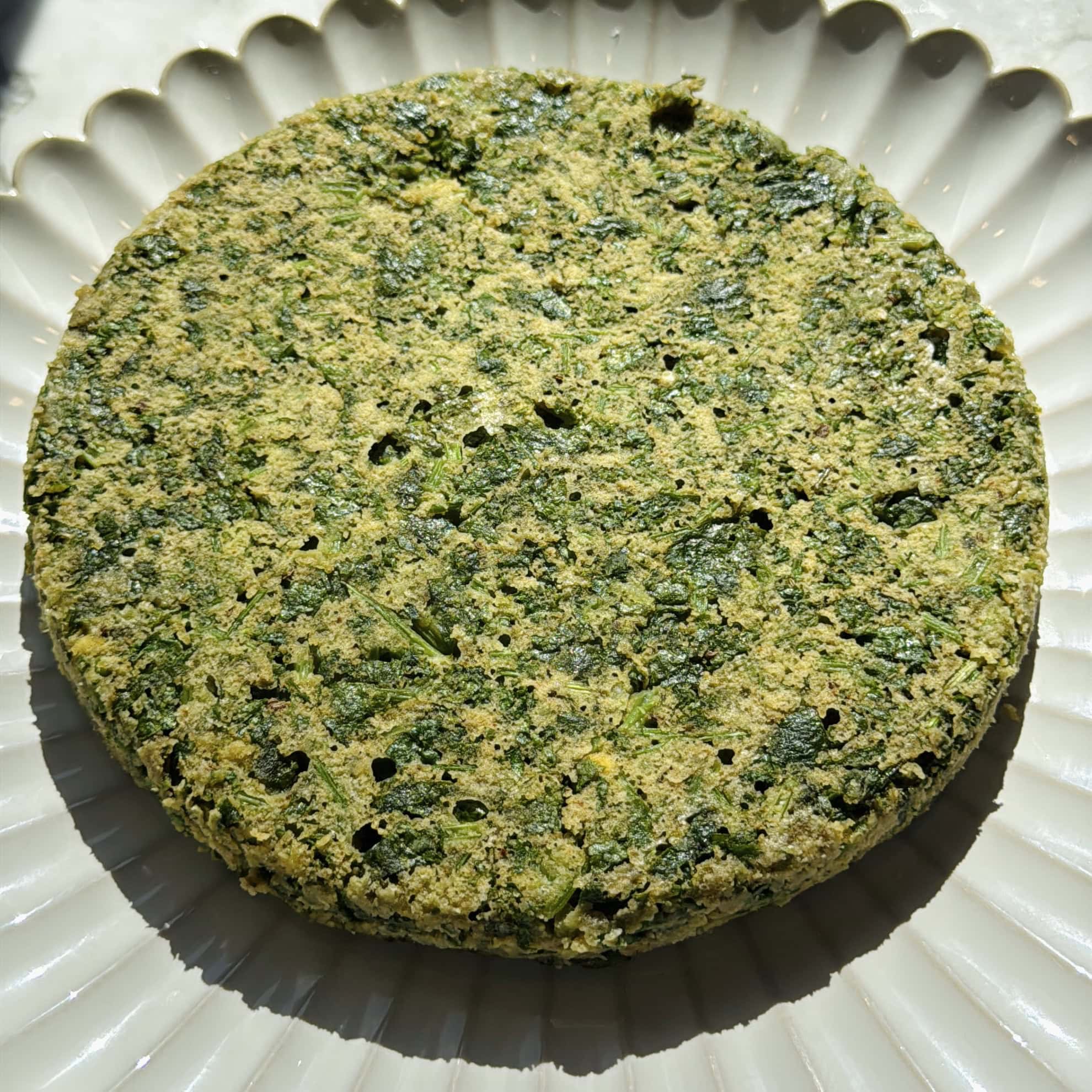 A round, kothimbitrvadi cake sits on a white, scalloped plate.