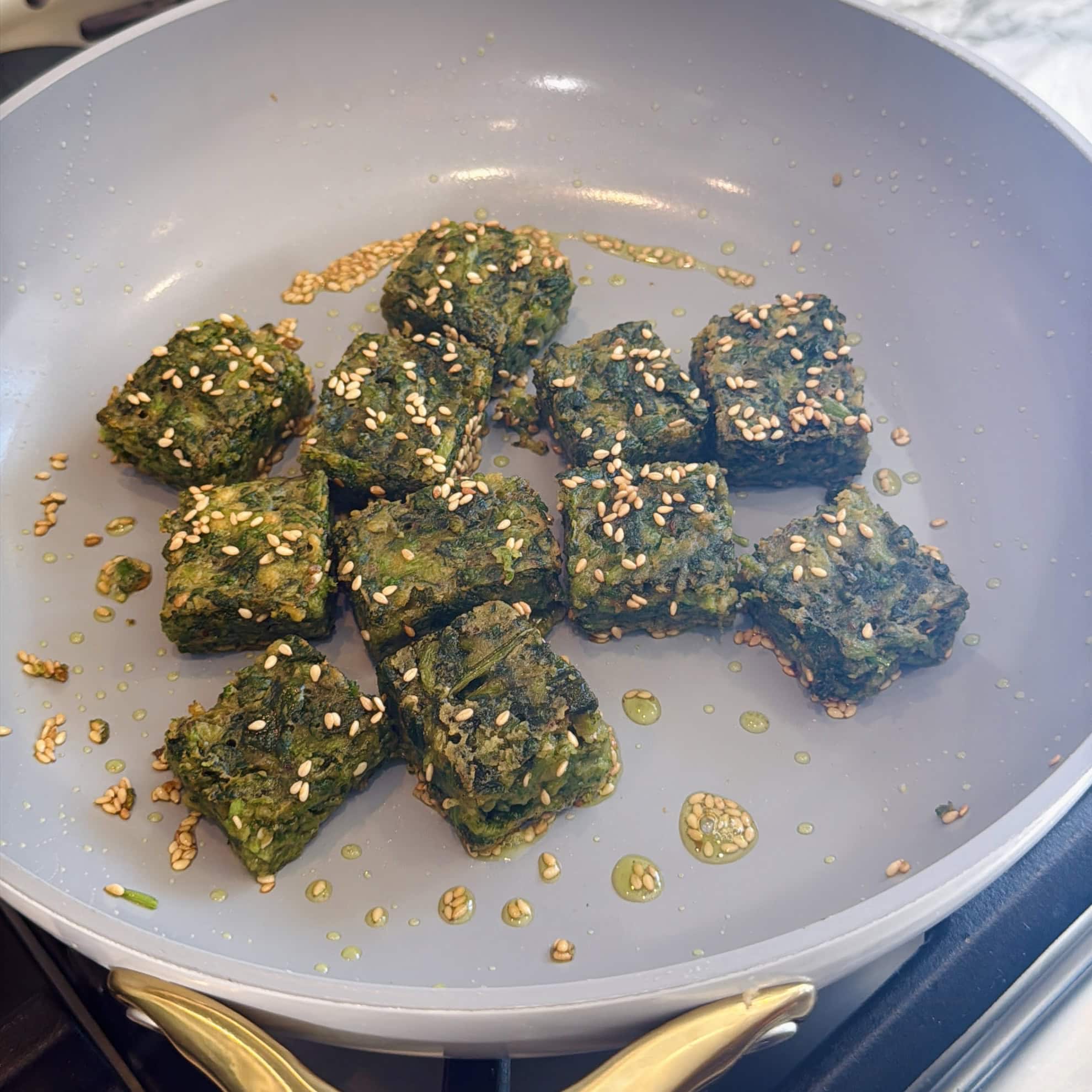 Pan fried Kothimbir with sesame seeds cooking in a gray non-stick pan on a stovetop.