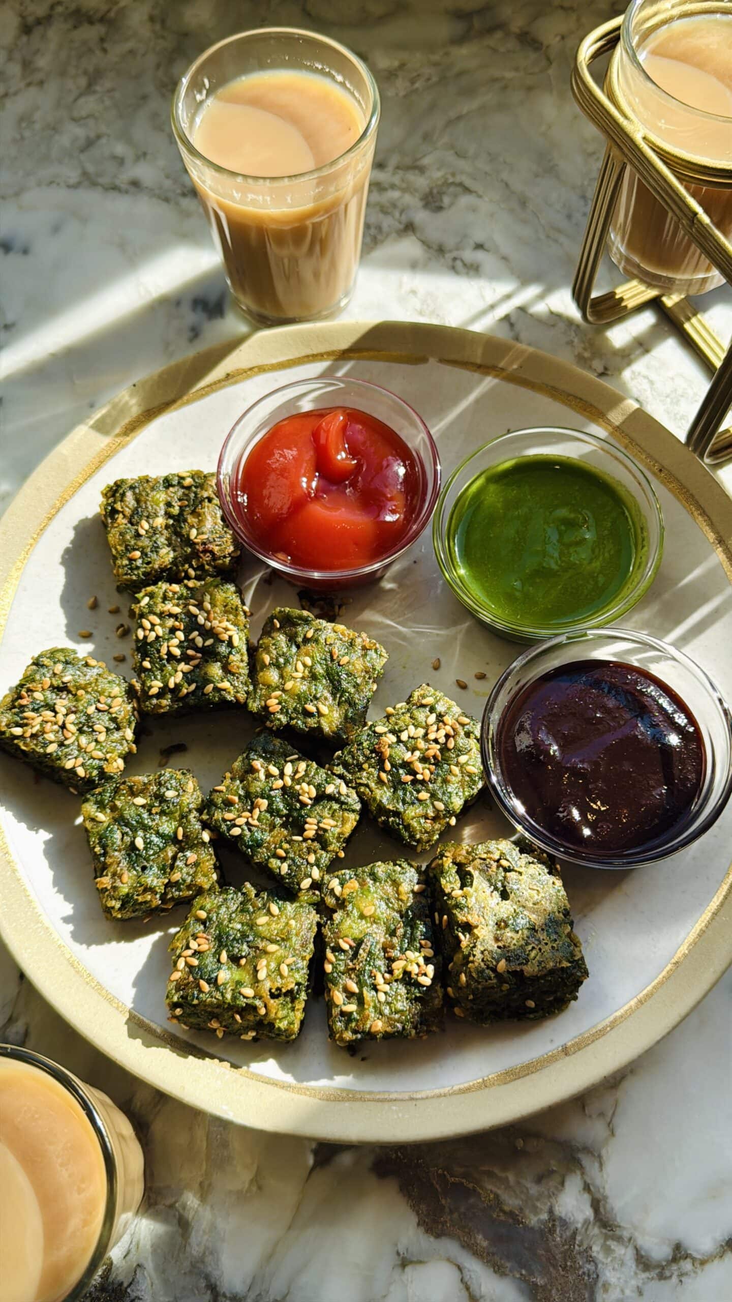 A plate with kothimbir vadi garnished with sesame seeds, served with ketchup, green chutney and tamarind chutney.