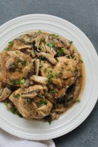White plate with chicken marsala garnished with chopped parsely