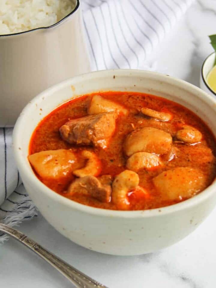 Thai Massaman Chicken Curry in a white bowl with sliced lime on the side