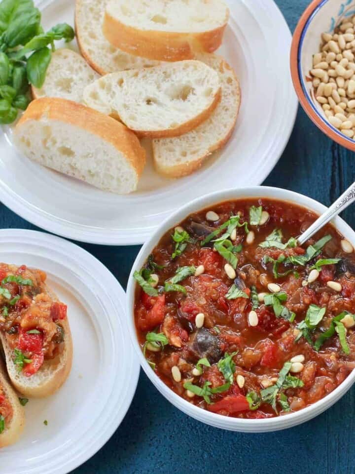 White Bowl with eggplant & red pepper spread, with sliced italian bread on the side in a white plate