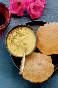 Dudhi Basundi in a bowl with puffed pooris served on the side