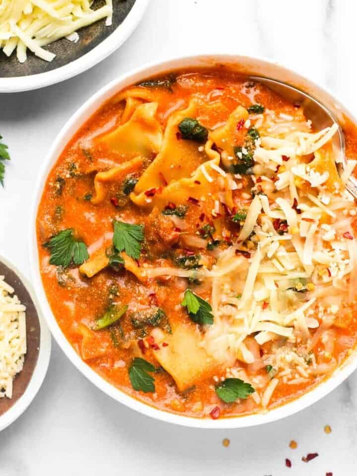 lasagna soup served in a white bowl, garnished with cheese and parsley