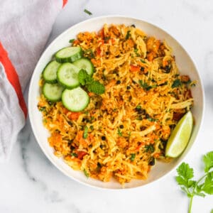 Keema Pulao served in a white bowl with cucumbers and lime wedge