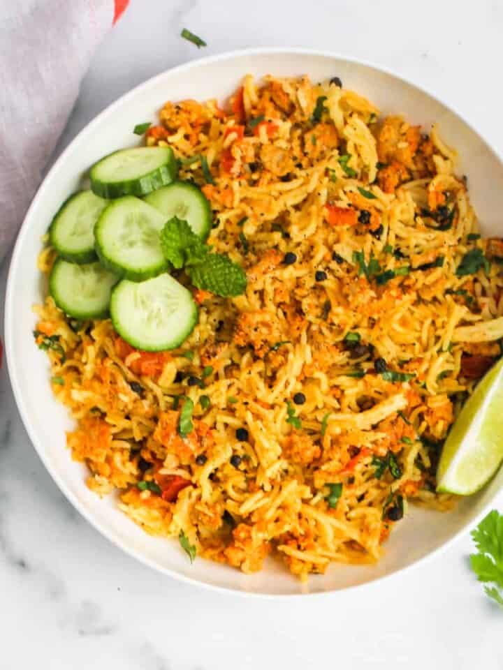 Keema Pulao served in a white bowl with cucumbers and lime wedge