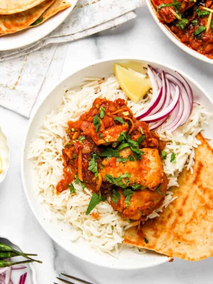 karahi chicken served over basmati rice along with naan, sliced onions and lemon wedge