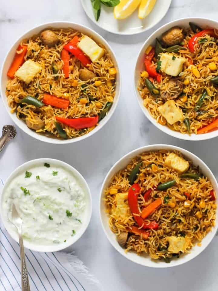 paneer and vegetable biryani served in 3 bowls with raita