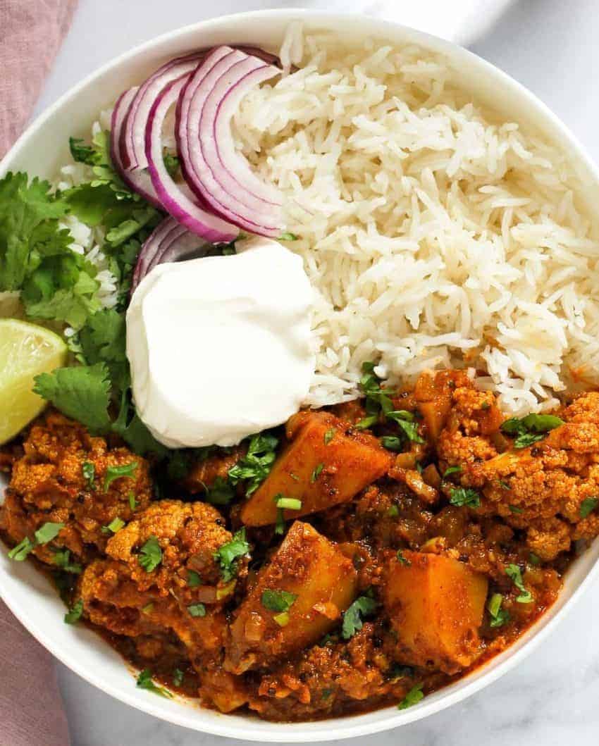 Cauliflower vindaloo curry served with rice, sliced onions and yogurt