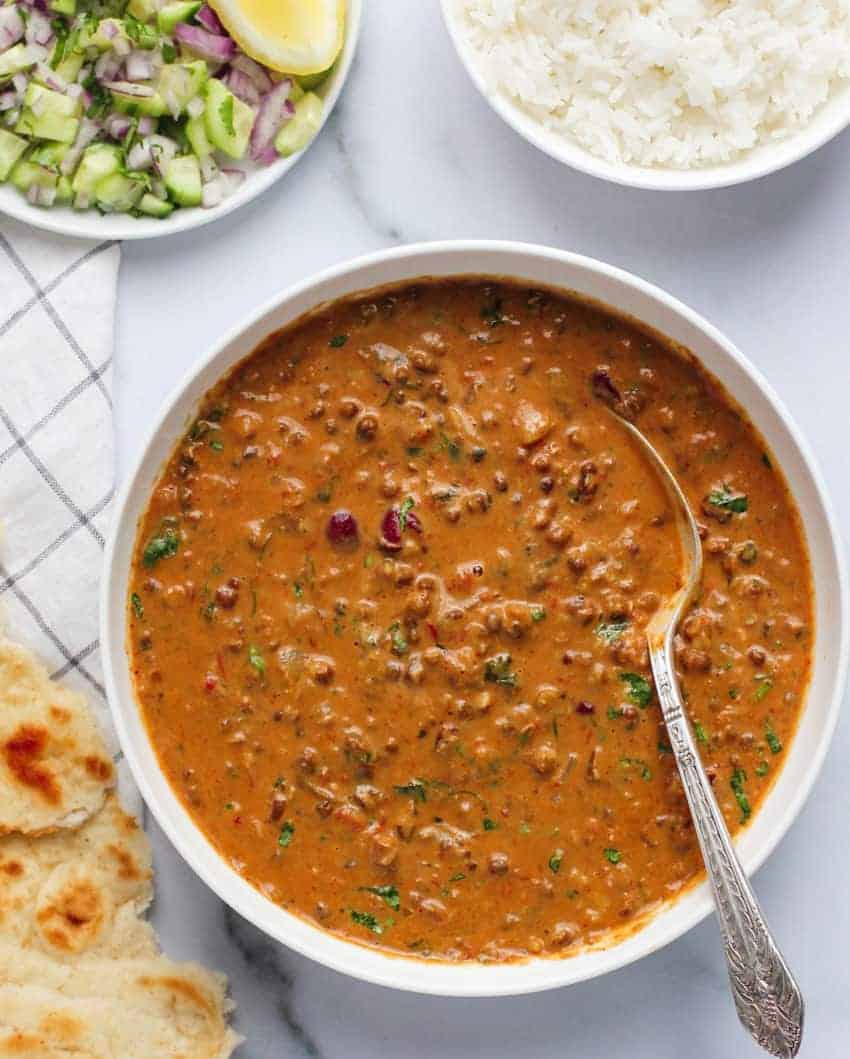 Daal Makhani served in a white bowl with rice, naan and raita on the side