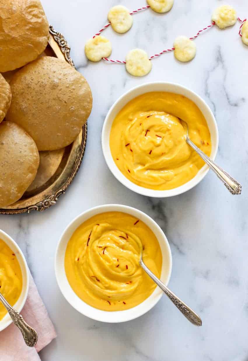 Mango Shrikhand in white bowls with Puri's on the side