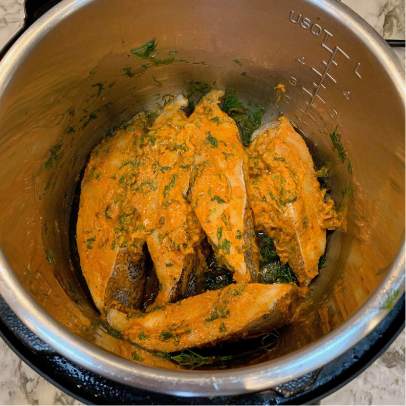 Fish fillets coated in yellow marinade with herbs placed inside a stainless steel pot, ready for cooking.